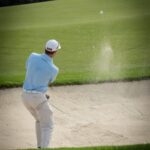Golfer swinging from sand trap on a sunny day at the golf course.