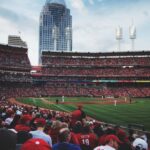 A vibrant scene at a baseball game in Cincinnati with a packed crowd and city skyline backdrop.